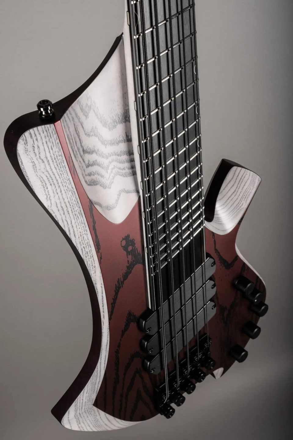 Ennea-H SN236, a headless bass: carved, beveled ash edges framing a deep red and black body